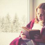 happy girl reading book by the window in winter